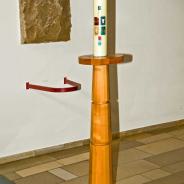 mit dem Grundstein der Kirche, darunter Ablage für den Deckel der Taufschale. Osterkerze